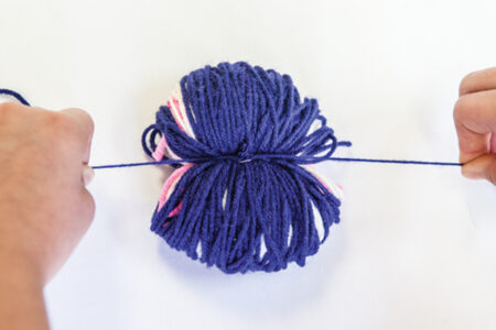person tying yarn around a wrapped ball of yarn